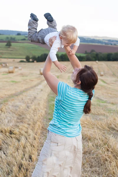 Jeune mère et son petit fils s'amusent dans un champ de paille — Photo