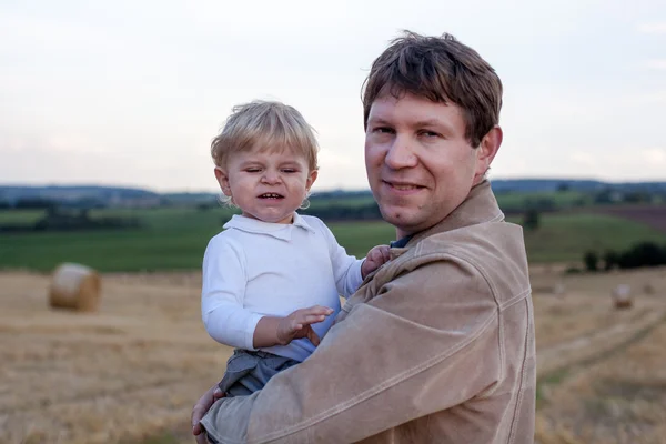 Молодой отец и очаровательный маленький сын обнимаются на соломенном поле — стоковое фото