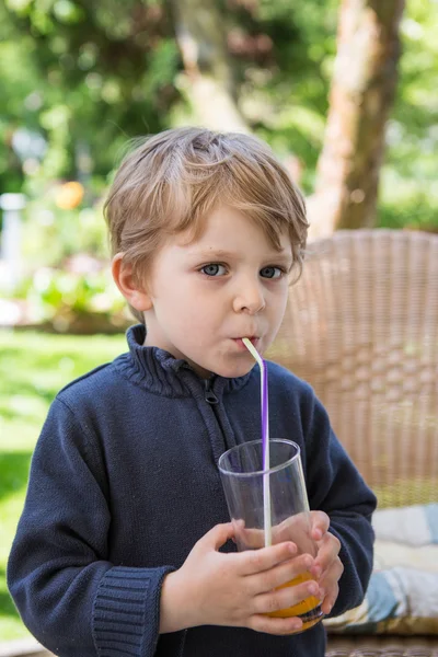 Glücklicher kleiner Junge trinkt Orangensaft mit Stroh — Stockfoto