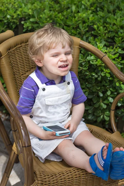 Pequeño niño rubio jugando con el teléfono celular — Foto de Stock