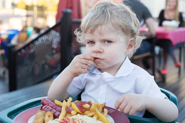 Cute little boy eating french fries in summer — Stock Photo, Image