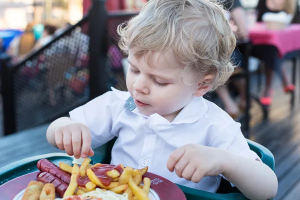 Bonito menino comendo batatas fritas no verão — Fotografia de Stock