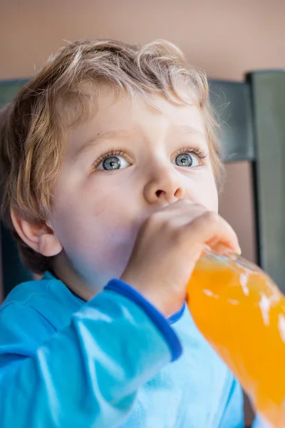 Fröhlicher kleiner Junge trinkt Orangensaft auf Balkon — Stockfoto