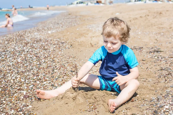 Little toddler boy playing with sand and stones on the beach — Stock Photo, Image