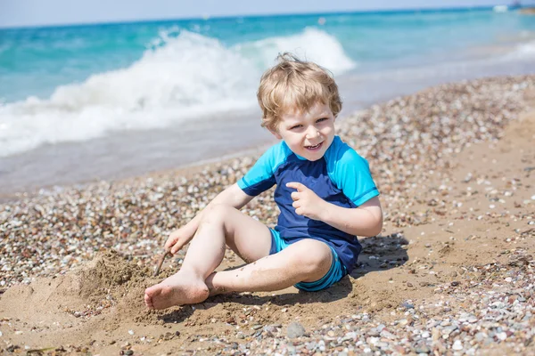 Little toddler boy playing with sand and stones on the beach — Stock Photo, Image