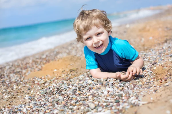 Pequeño niño jugando con arena y piedras en la playa — Foto de Stock