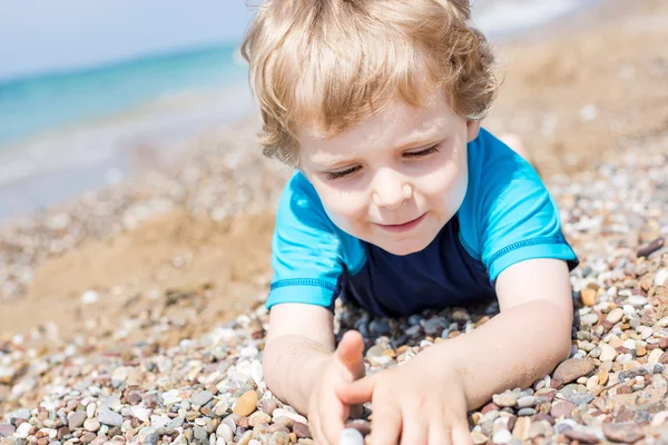 Little toddler boy playing with sand and stones on the beach — Stock Photo, Image