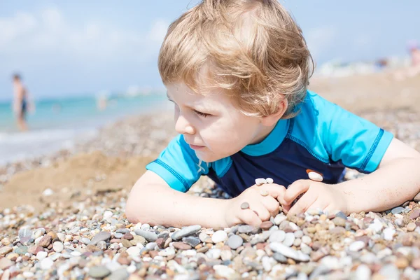 Pequeño niño jugando con arena y piedras en la playa — Foto de Stock