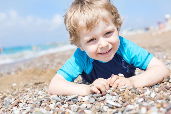 Kleiner Junge spielt mit Sand und Steinen am Strand — Stockfoto