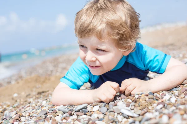 Kleiner Junge spielt mit Sand und Steinen am Strand — Stockfoto