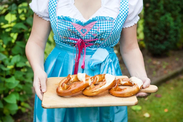 Glücklich schöne Frau im Dirndl hält Brezel — Stockfoto