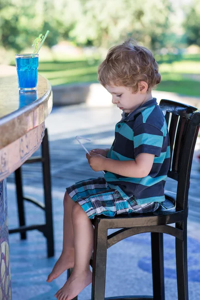 Little blond boy sitting on high chair in cafe with cocktail — Stock Photo, Image