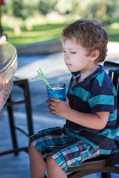 Маленький блондин, сидящий на стуле в кафе с коктейлем — стоковое фото