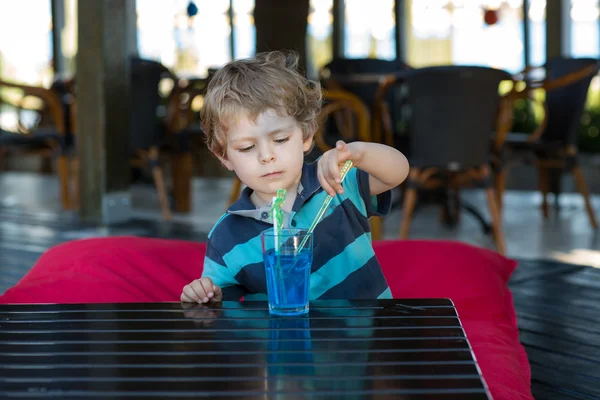 Pequeño chico rubio sentado en la silla alta en la cafetería con cóctel — Foto de Stock