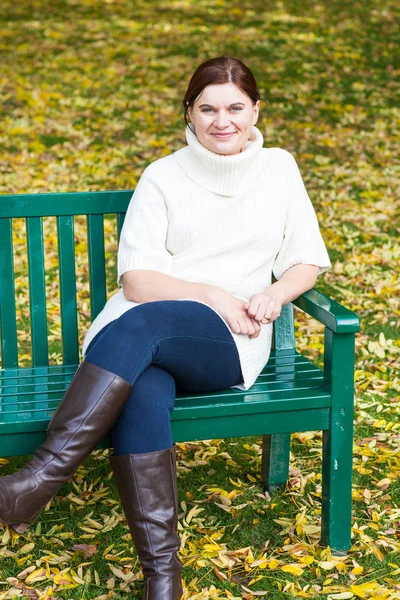 Krásná žena v podzimním parku sedí na lavičce — Stock fotografie