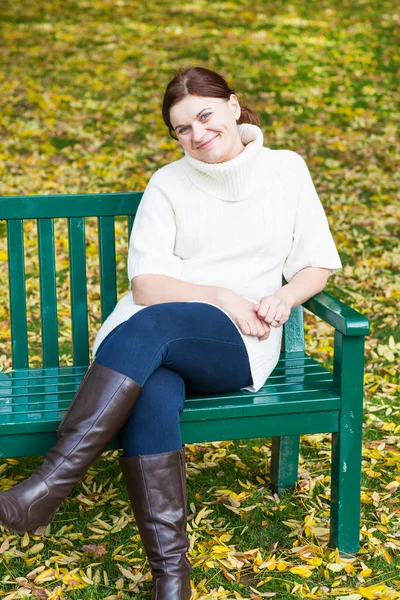 Schöne Frau im herbstlichen Park auf Bank sitzend — Stockfoto