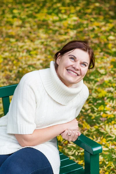 Vacker kvinna i parken höst sitter på bänken — Stockfoto