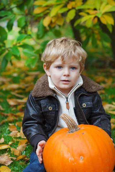 Kleine peuter met grote oranje pompoen in tuin — Stockfoto