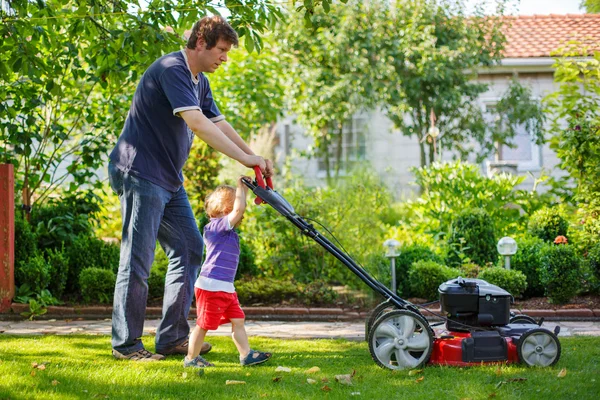 Mannen och hans lille son har roligt med gräsklippare i trädgården — Stockfoto