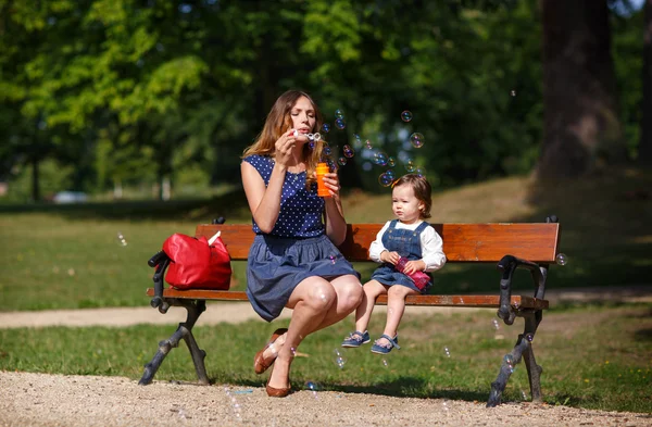 Beautiful mother and adorable daughter blowing soap bubbles in sum — Stock Photo, Image