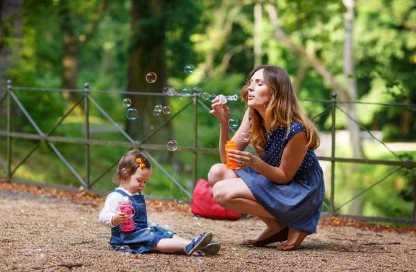 Schöne Mutter und kleine Tochter pusten Seifenblasen in Summe — Stockfoto