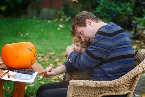 Hombre joven y niño pequeño haciendo calabaza de halloween — Foto de Stock