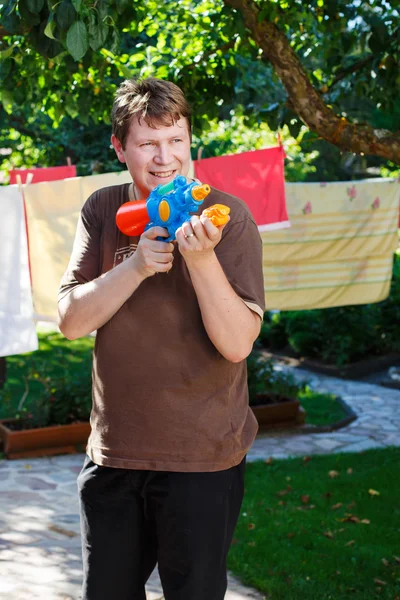 Ung man leker med vattenpistol i sommarträdgård — Stockfoto