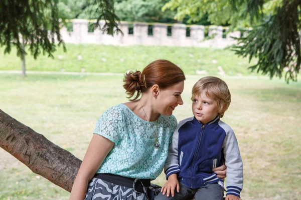 Young woman sitting on tree with her little son and speaking — Stock Photo, Image