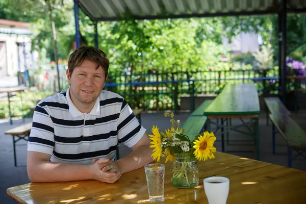 Young man sitting in country cafe and drinking coffee and water — Stock Photo, Image