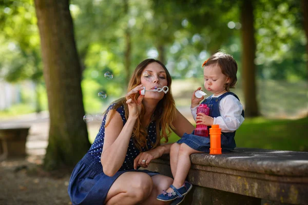 Красивая мать и маленькая дочь, надувающие мыльные пузыри в сумме — стоковое фото
