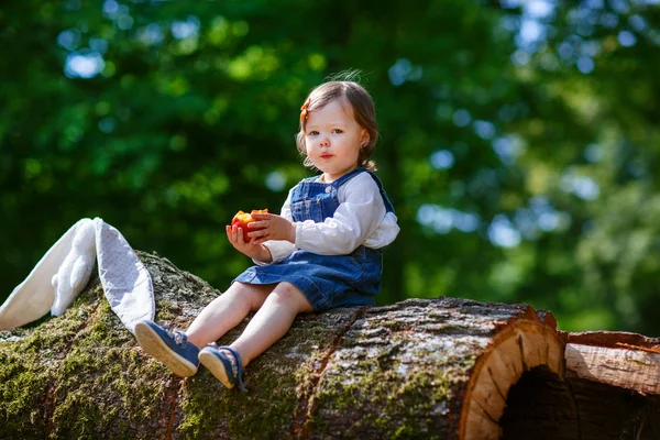 Lilla söta flicka äter frukt i skogen — Stockfoto