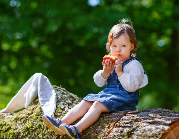 Kis aranyos baba lány eszik gyümölcsöt az erdő — Stock Fotó