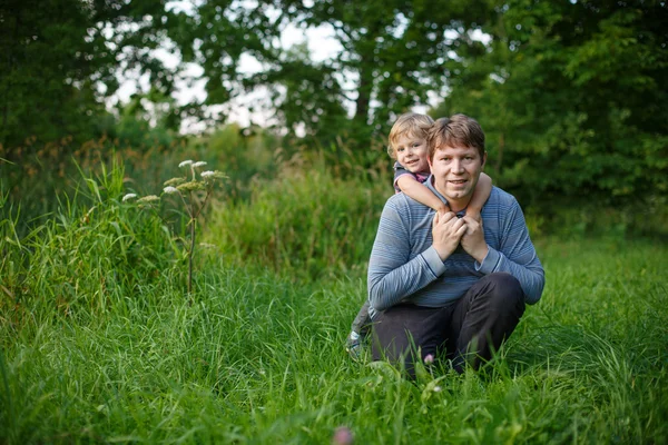 Little boy and his father sitting on grass in summer forest — Stock Photo, Image