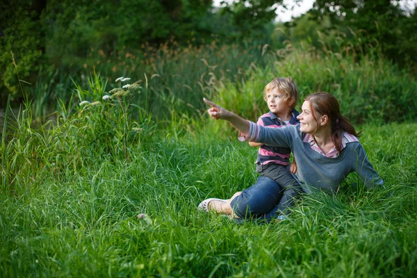 Liten pojke och hans mor som sitter på gräset i sommar skog — Stockfoto