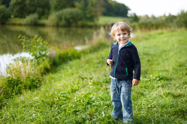 Lille blond dreng nær skov sø, på sommeraften - Stock-foto