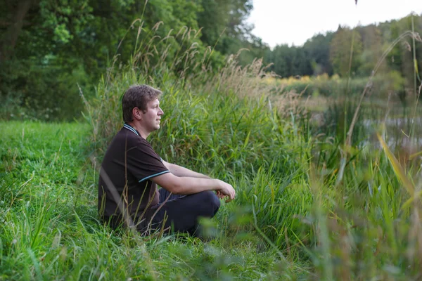 Jeune homme beau assis près du lac de la forêt et relaxant — Photo