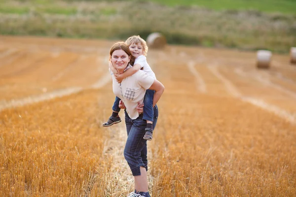 Junge Mutter und ihr kleiner Sohn amüsieren sich auf gelbem Heufeld — Stockfoto