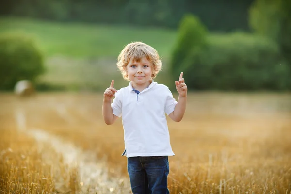 Sevimli sarışın küçük çocuk sarı saman sahada eğleniyor — Stok fotoğraf