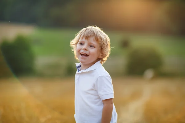 Felice bambino biondo divertirsi sul campo di fieno giallo — Foto Stock