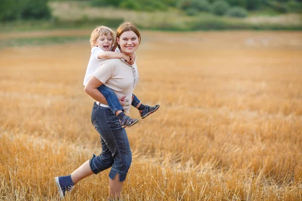 Молодая мать и ее маленький сын веселятся на желтом сеновале — стоковое фото