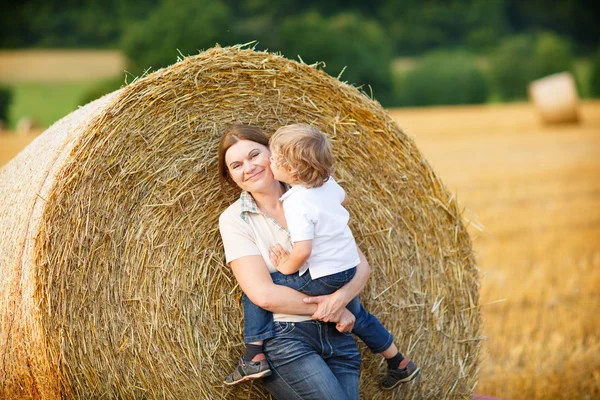 Junge Mutter und ihr kleiner Sohn amüsieren sich auf gelbem Heufeld — Stockfoto