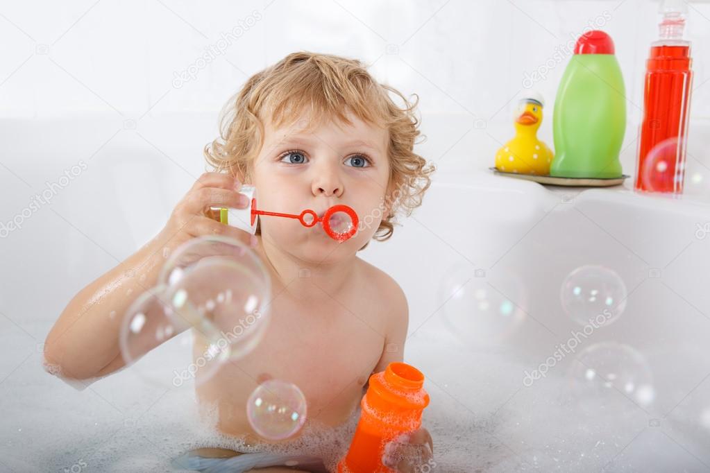 Adorable blond toddler boy playing with soap bubbles in bathtub