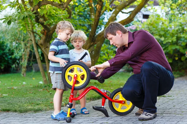 Joven y dos hijos pequeños reparando la bicicleta al aire libre . —  Fotos de Stock