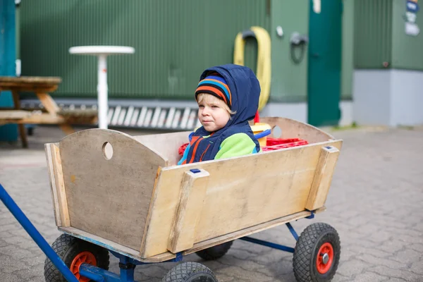Cute toddler boy of two years in wooden trolley in autumn clothe — Stock Photo, Image