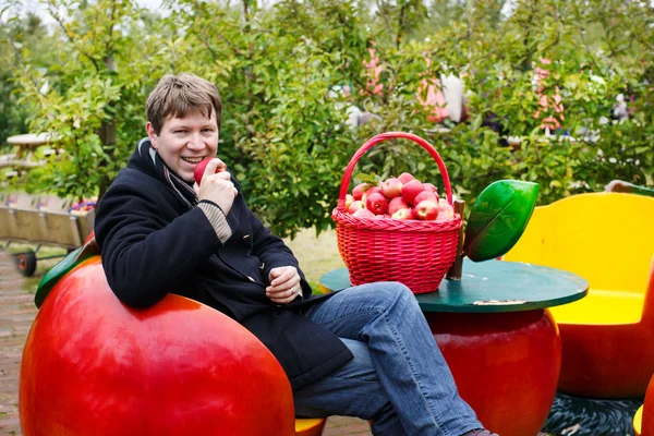 Jeune homme mangeant des pommes rouges dans un verger — Photo