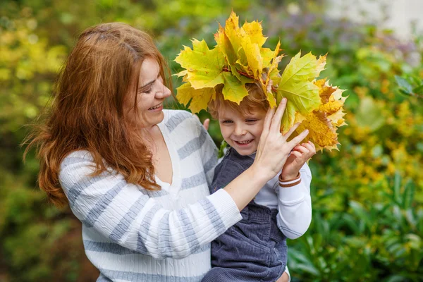 Giovane madre in una ghirlanda di foglie d'acero che tiene piccolo bambino ragazzo — Foto Stock