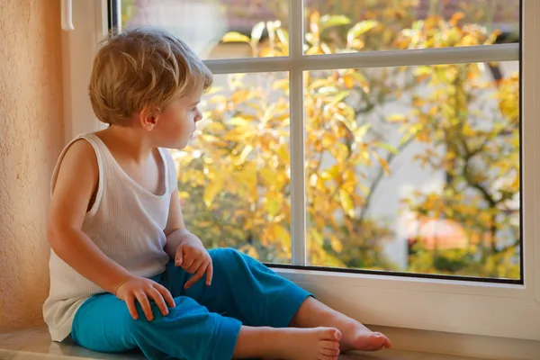 Precioso chico de dos años mirando por la ventana en amarillo autu — Foto de Stock