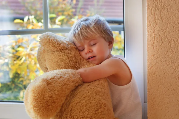 Precioso niño de dos años sentado cerca de la ventana con gran oso de juguete . — Foto de Stock