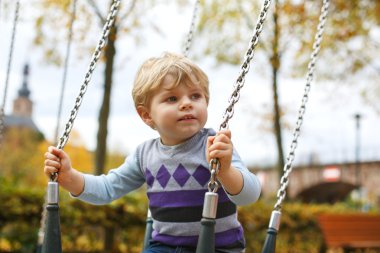 Küçük tatlı çocuk zincirli salıncaklarda eğleniyor.