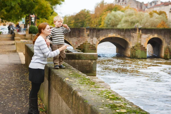 Roztomilý malý syn a matka v podzimní city. — Stock fotografie